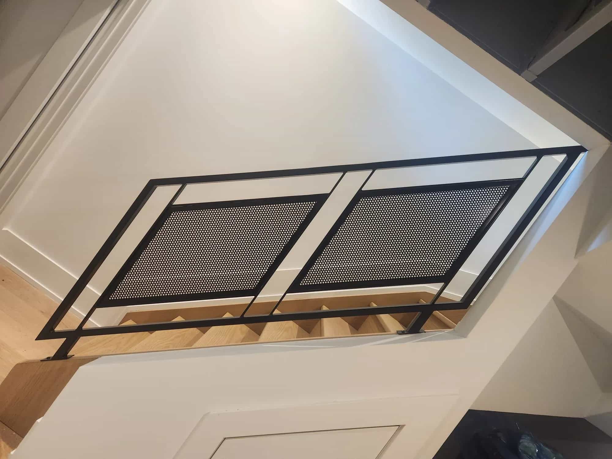 Two black steel frames filled with perforated metal panels guarding the edge of a stairwell, seen from the landing below