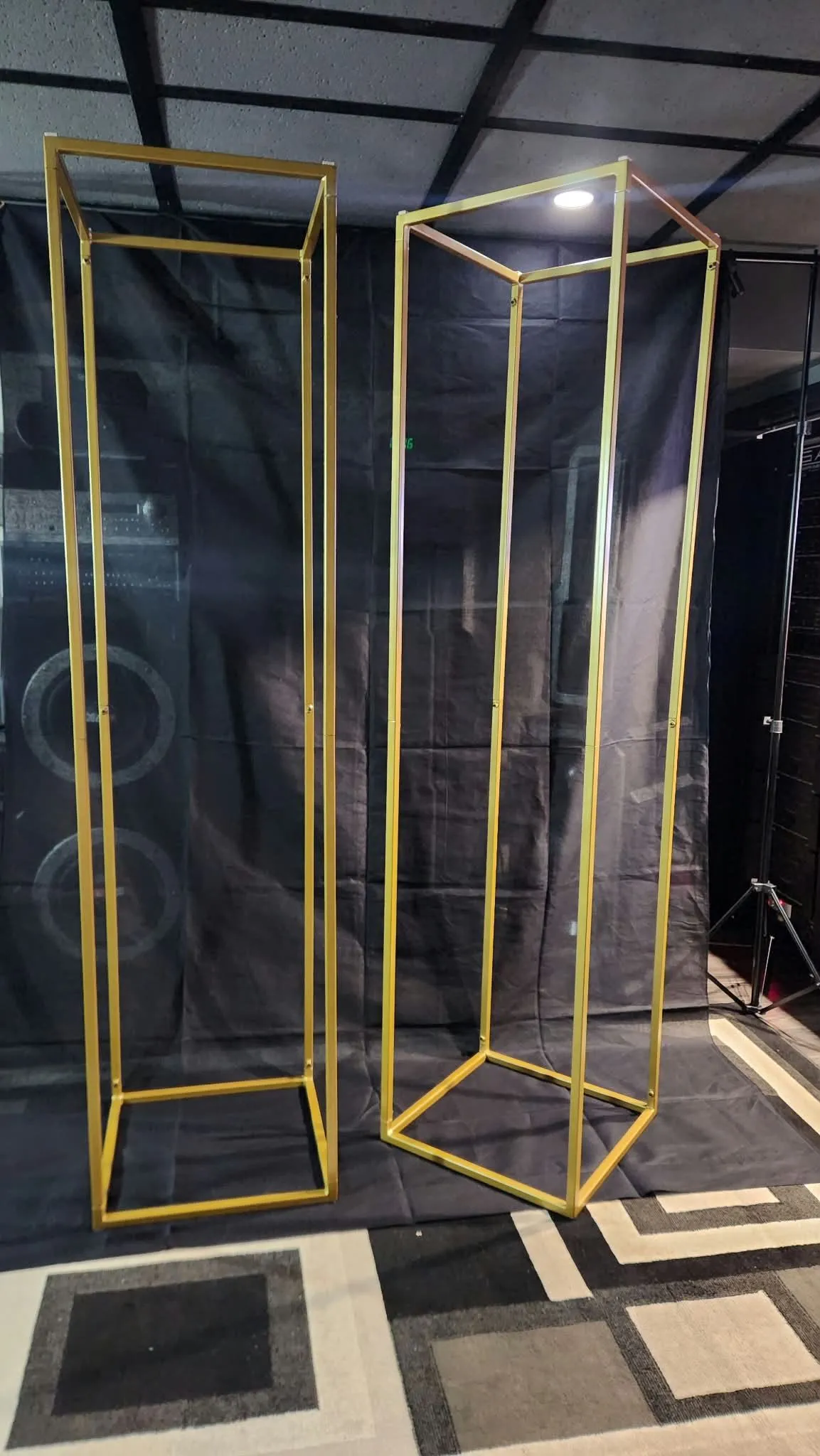 Two tall rectangular metal frames with a gold finish standing in front of a black fabric backdrop
