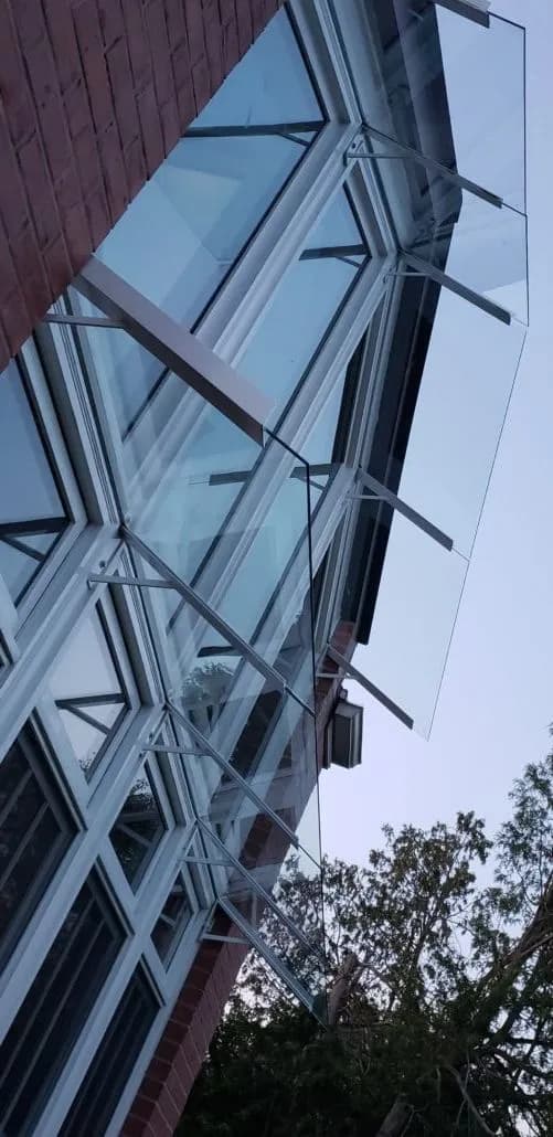 Glass canopy panels carried on angled steel arms fixed to a brick wall above an entrance, seen from below