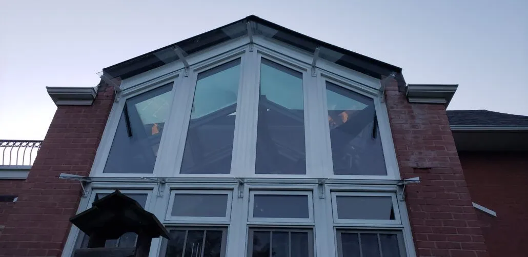 Black steel canopy frame below a tall three-storey window wall on a red brick building