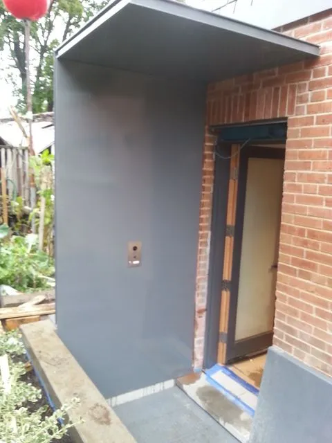 Grey flat metal canopy projecting over a side door on a brick house
