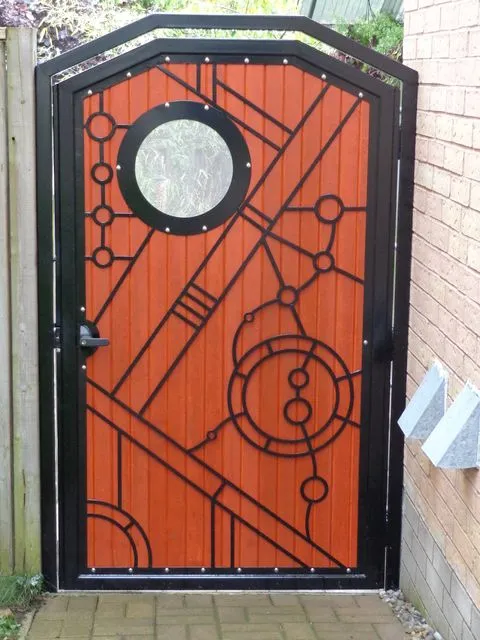Arched black steel gate with circles, diagonals, and a round porthole window over reddish wood panels in a side passage