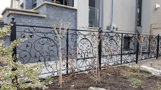 Black iron fence with dense scroll panels between square posts along a newly planted front garden