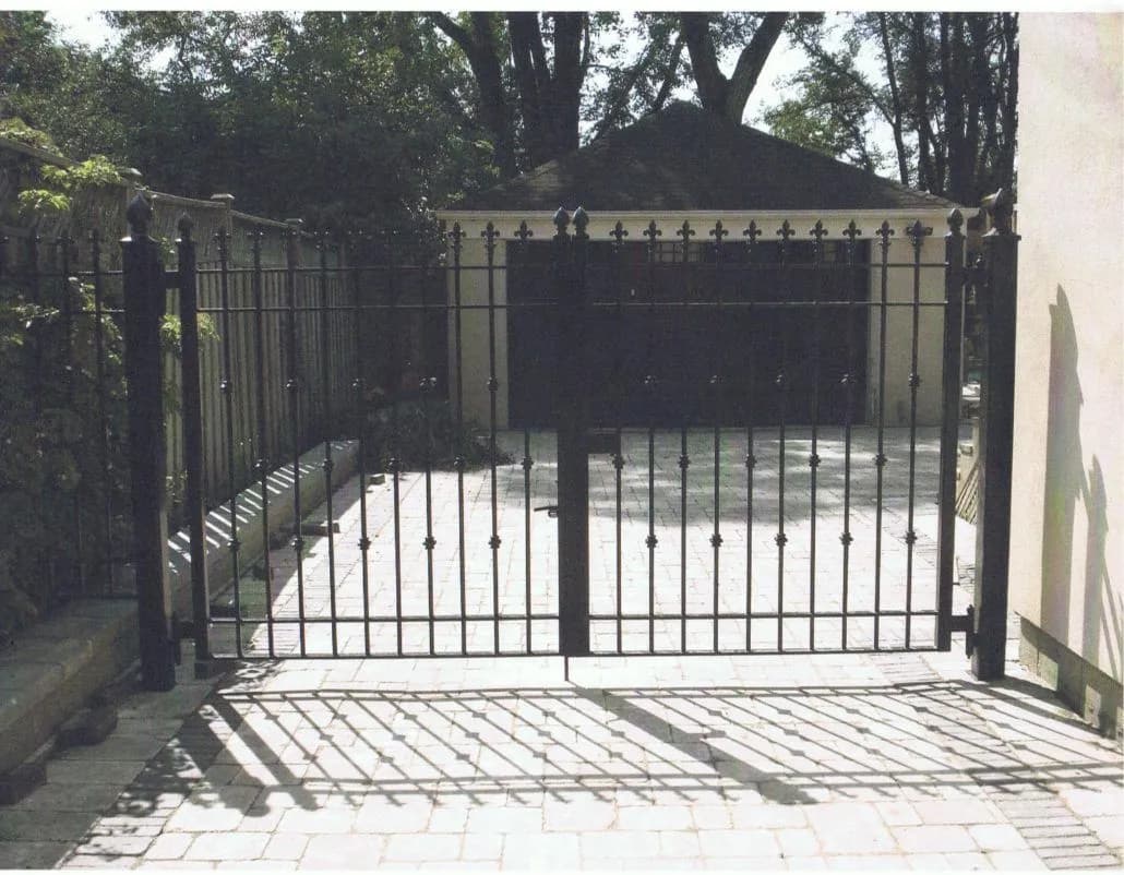 Black steel double gate and fence with finial-topped pickets closing an interlock driveway in front of a garage