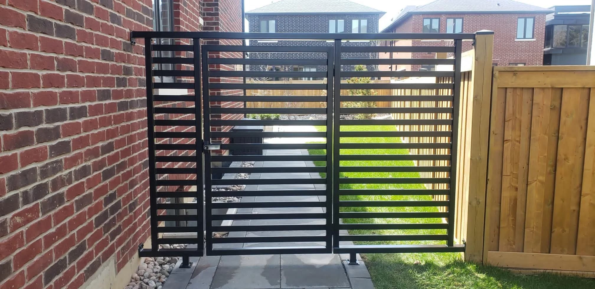 Black horizontal slat gate and matching fence panel between a brick wall and a wood privacy fence