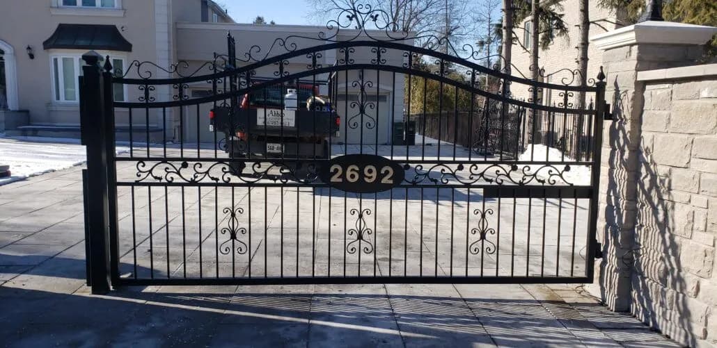 Black arched double driveway gate with scrollwork and spear tops hung between stone pillars