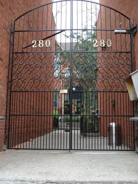 Tall arched black iron gate with scroll panels and pickets set into a brick archway