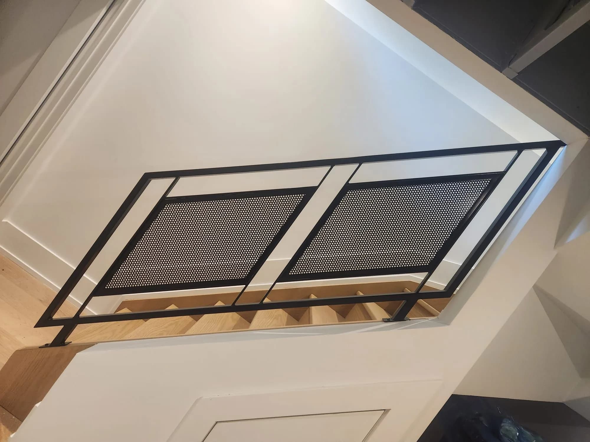 Two black steel frames filled with perforated metal panels guarding the edge of a stairwell, seen from the landing below