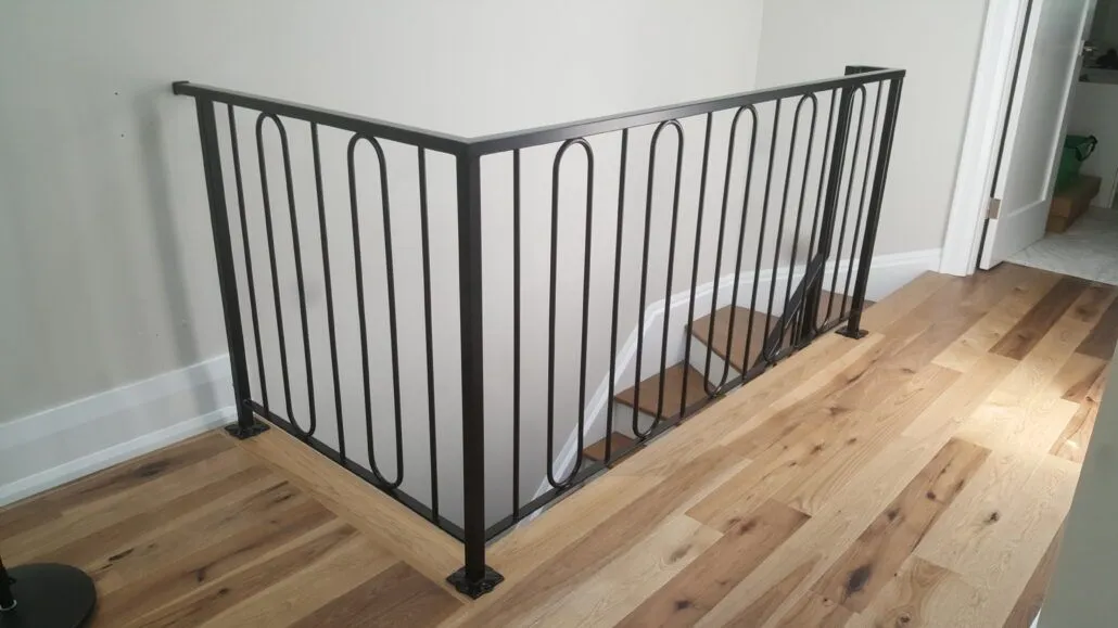 Black steel railing with alternating straight and looped balusters guarding a stair opening on a wide-plank oak floor