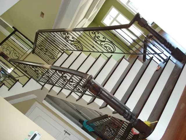 Black wrought iron scroll panels under a stained wood handrail following a curved staircase with white risers