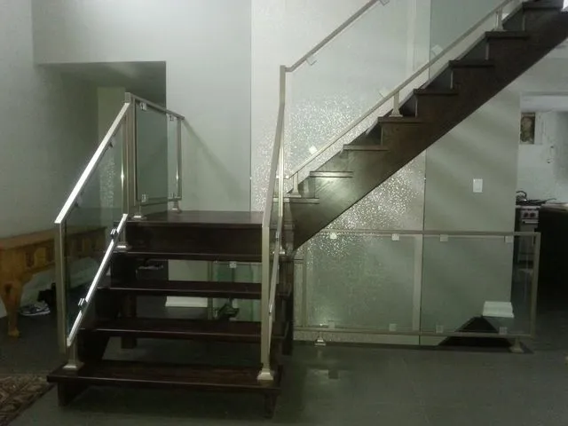 Clear glass panels with stainless steel posts and handrail running up a staircase with dark wood treads
