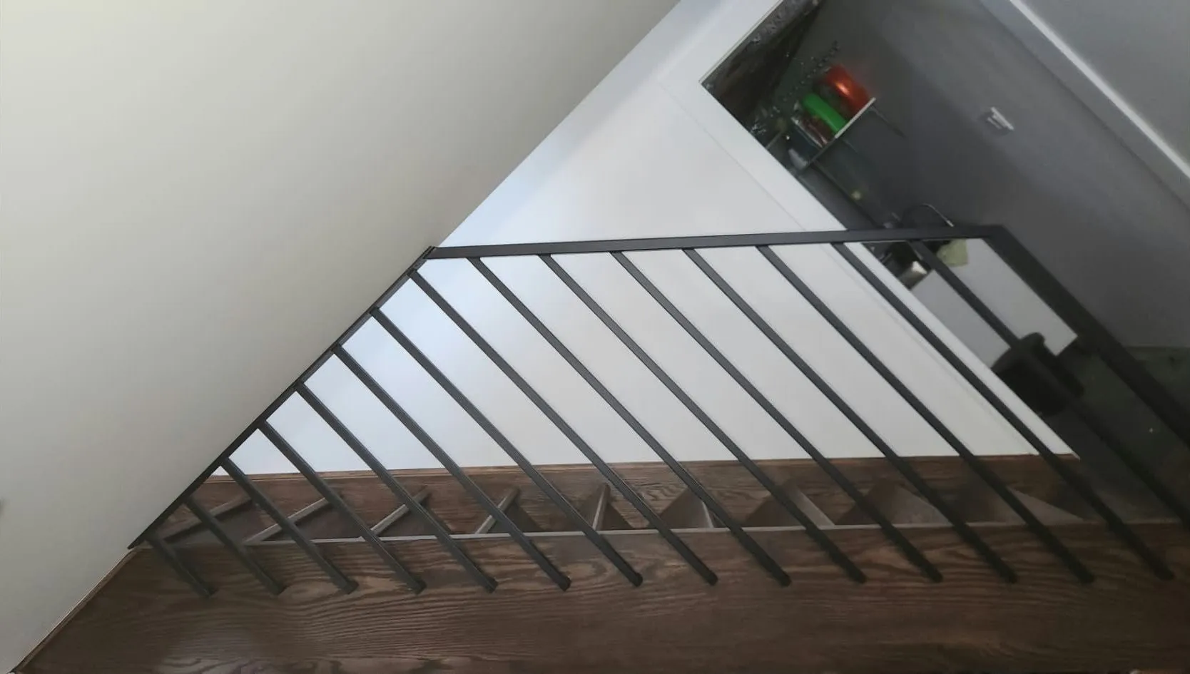 Black metal guard with slim angled pickets along the edge of a staircase with dark wood treads, photographed from below