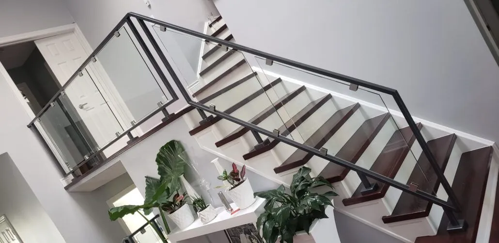 Frameless glass guard with a black metal handrail along a landing above a dark wood staircase