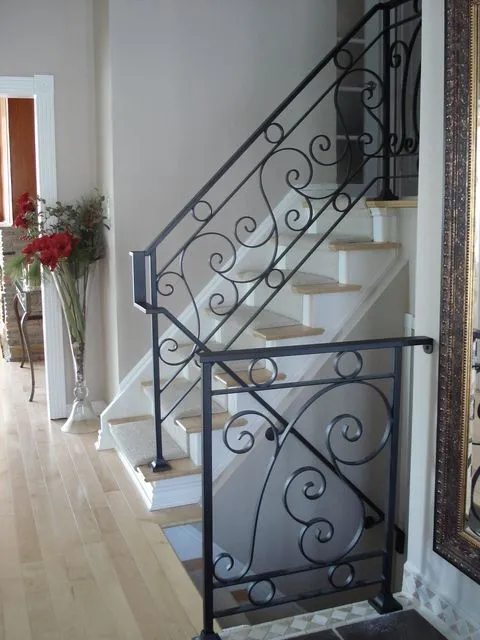 Black scrolled iron stair railing curving down to a volute at the bottom step beside a white staircase