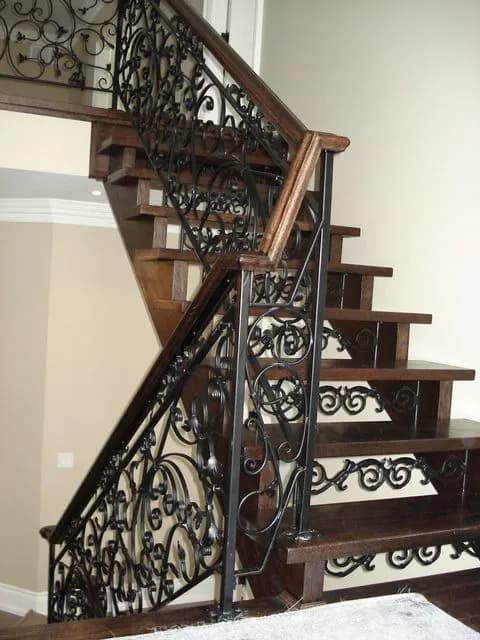 Black wrought iron railing with dense scrollwork panels running up a dark wood staircase