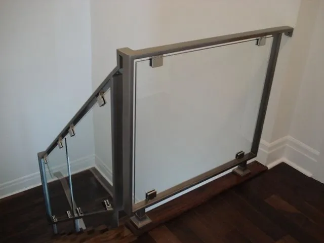 Glass panel guard held by brushed metal clamps under a wood-capped rail at an interior landing