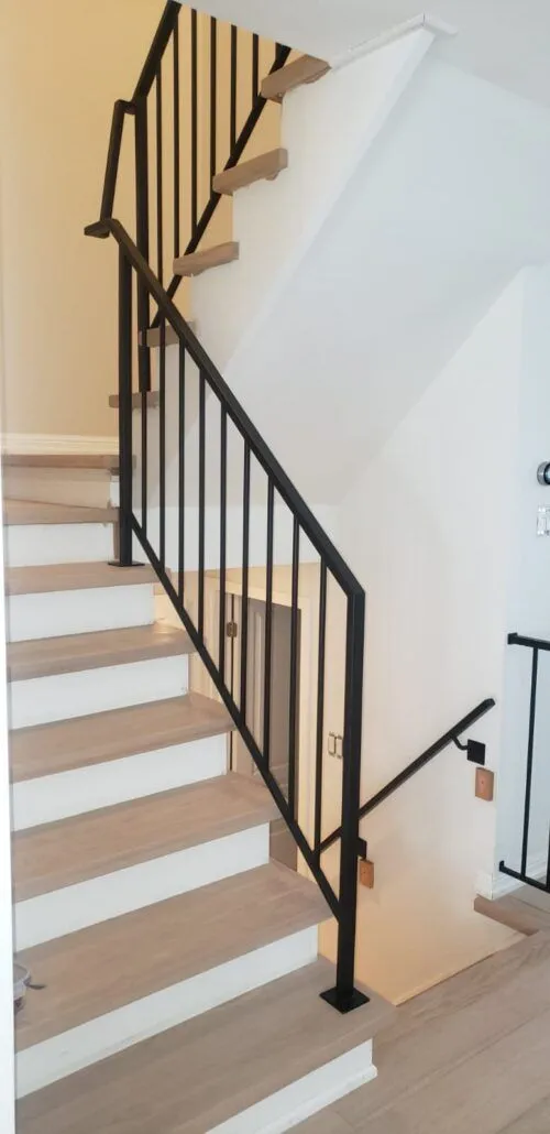 Slim black picket stair railing with a square top rail running along white painted treads and risers