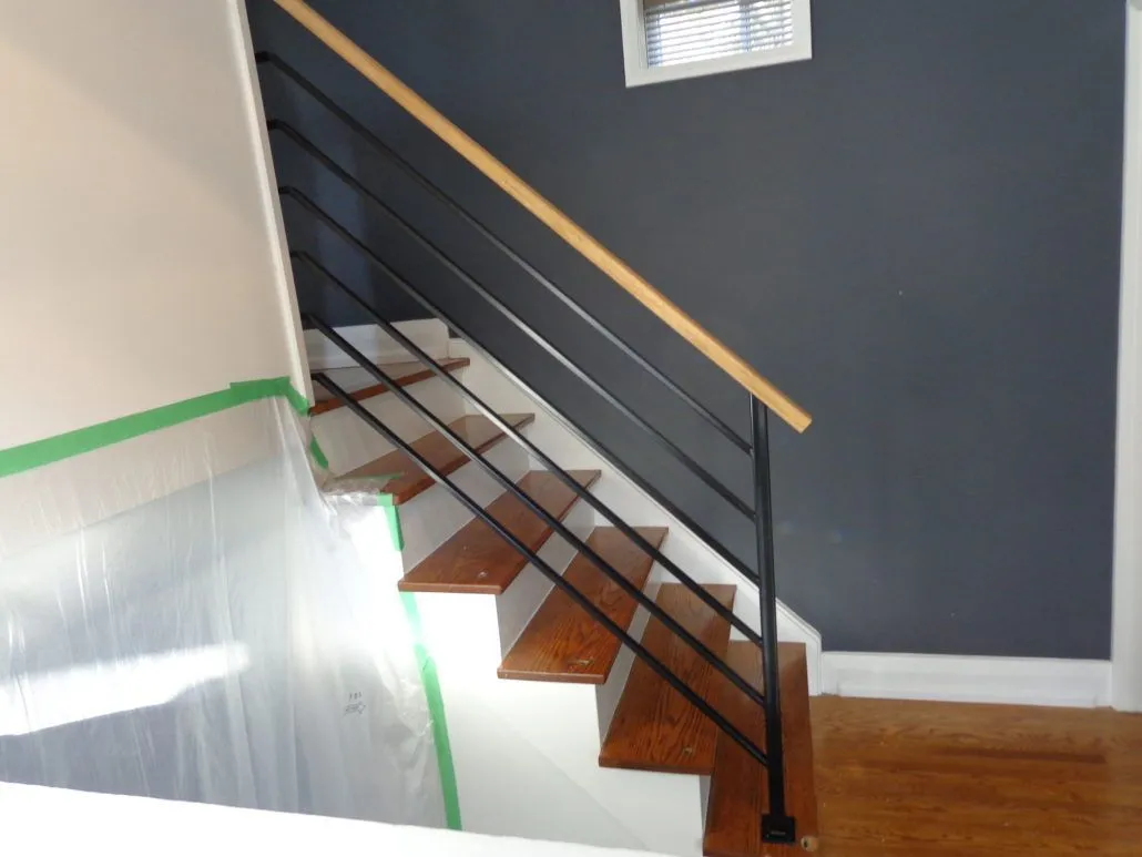 Black horizontal bar stair railing with a wood handrail along wood treads by a dark accent wall