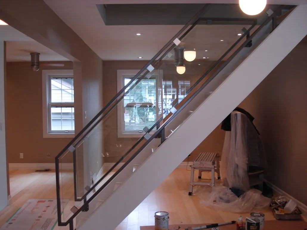 Glass stair guard with a dark metal cap rail beside a staircase in a room being finished