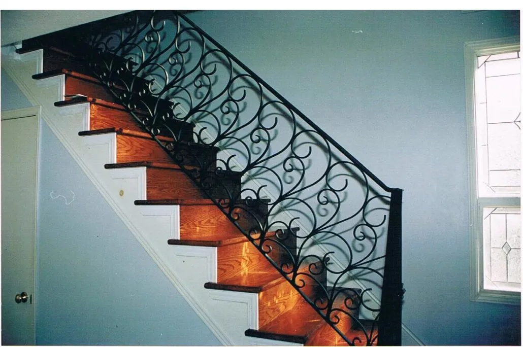 Black ornate scrollwork stair railing with dense curls beside wood treads and a painted wall