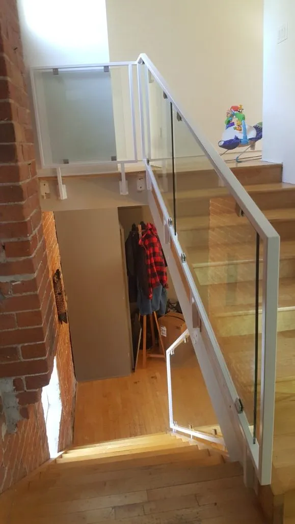 Glass stair guard with a metal cap rail beside an open basement staircase in a hallway