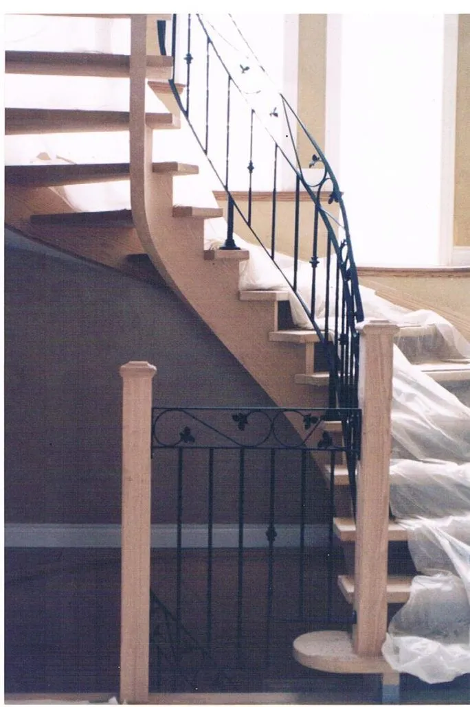 Black iron balusters with scroll detail set between wood newel posts on a curved staircase