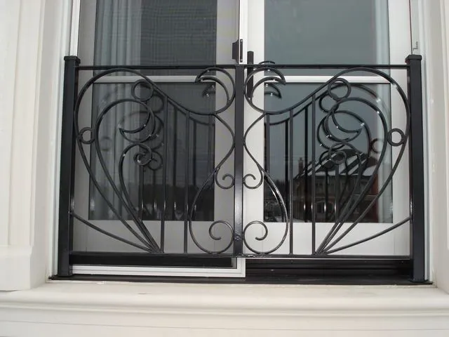 Black iron Juliet railing with mirrored heart-shaped scrolls fixed across a white French door opening