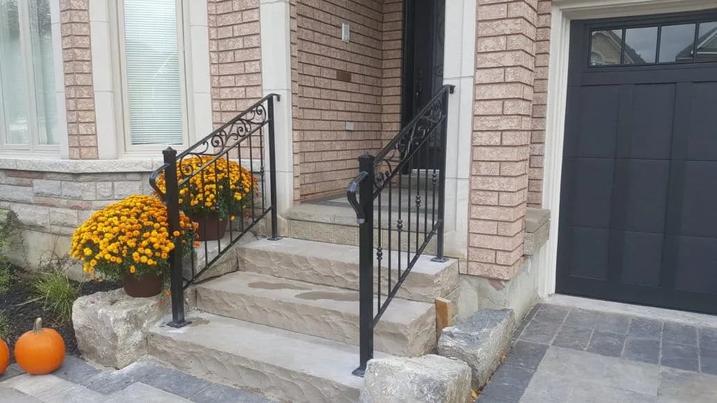 Pair of black iron step railings with scrolled top panels on natural stone steps beside a front door