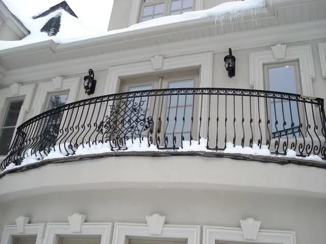 Black wrought iron railing with scroll and lattice details following a curved stone balcony above a front entrance