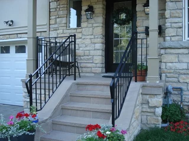 Black steel porch guard and step railings on a stone-clad front porch with columns and red flowers