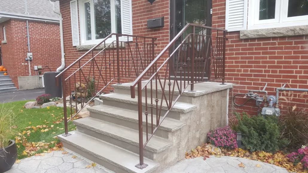 Bronze-coloured steel railing with X-pattern panels on both sides of concrete front steps outside a brick bungalow