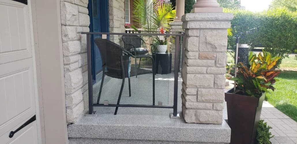 Simple black iron railing enclosing a small front porch between cut-stone columns, with a patio chair and planters