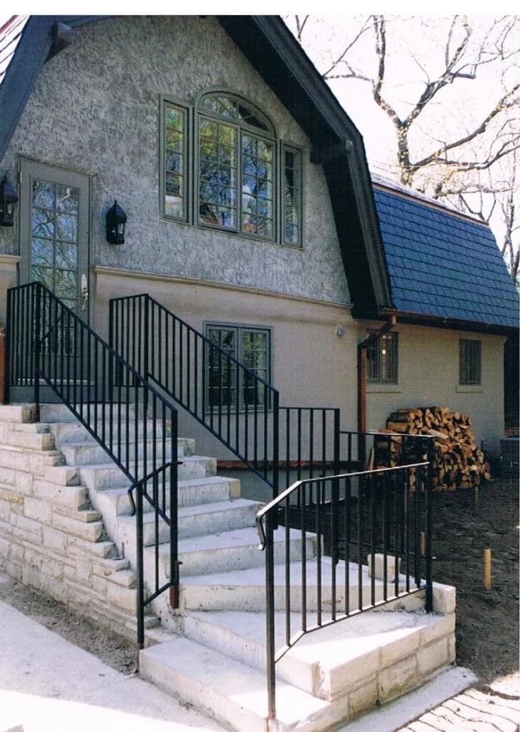 Black steel picket railings on both sides of a wide stone staircase and landing at the side of a new house