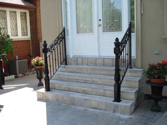 Black iron porch railings with scroll panels and heavy cast newel posts flanking stone steps to a front door