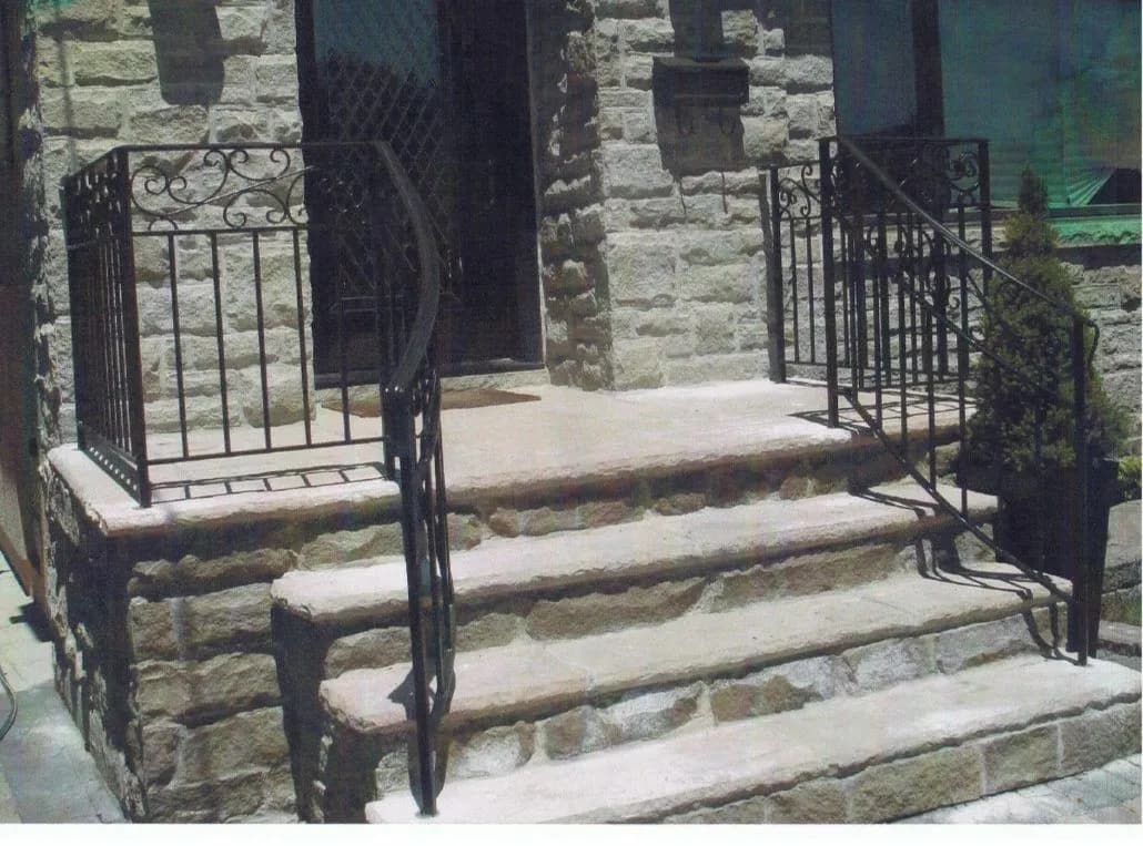 Black ornamental iron gate and matching step railings with scroll tops on wide stone steps