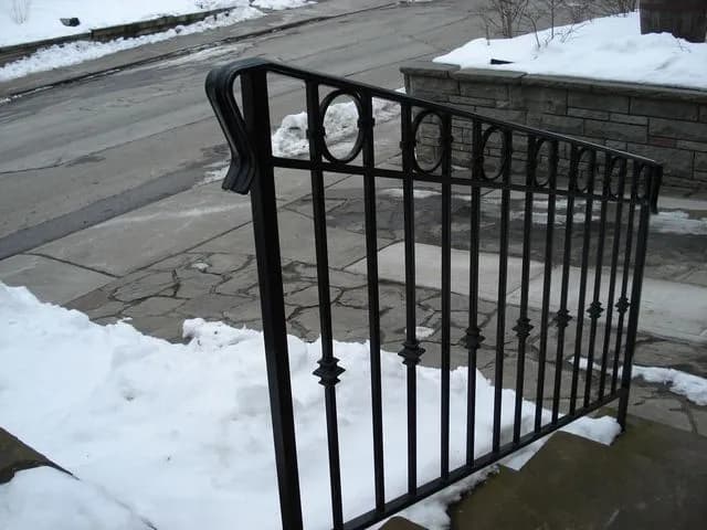 Black ornamental iron railing with ring and spear details along stone steps in the snow
