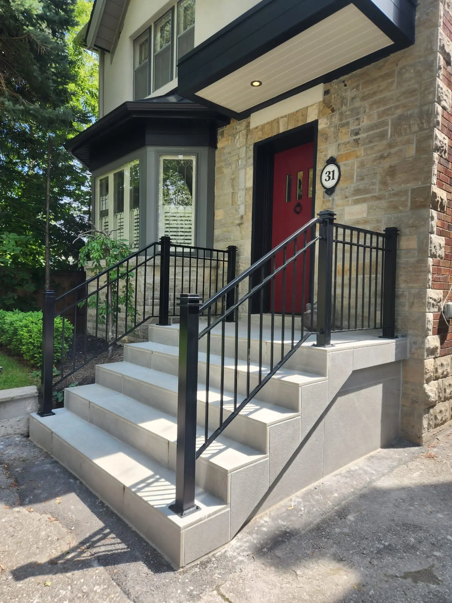 Black metal railings with square posts on concrete front steps leading up to a red front door