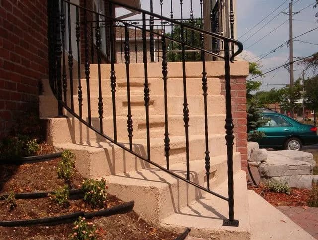Black ornamental railing with knuckle-detailed balusters curving along stone entrance steps
