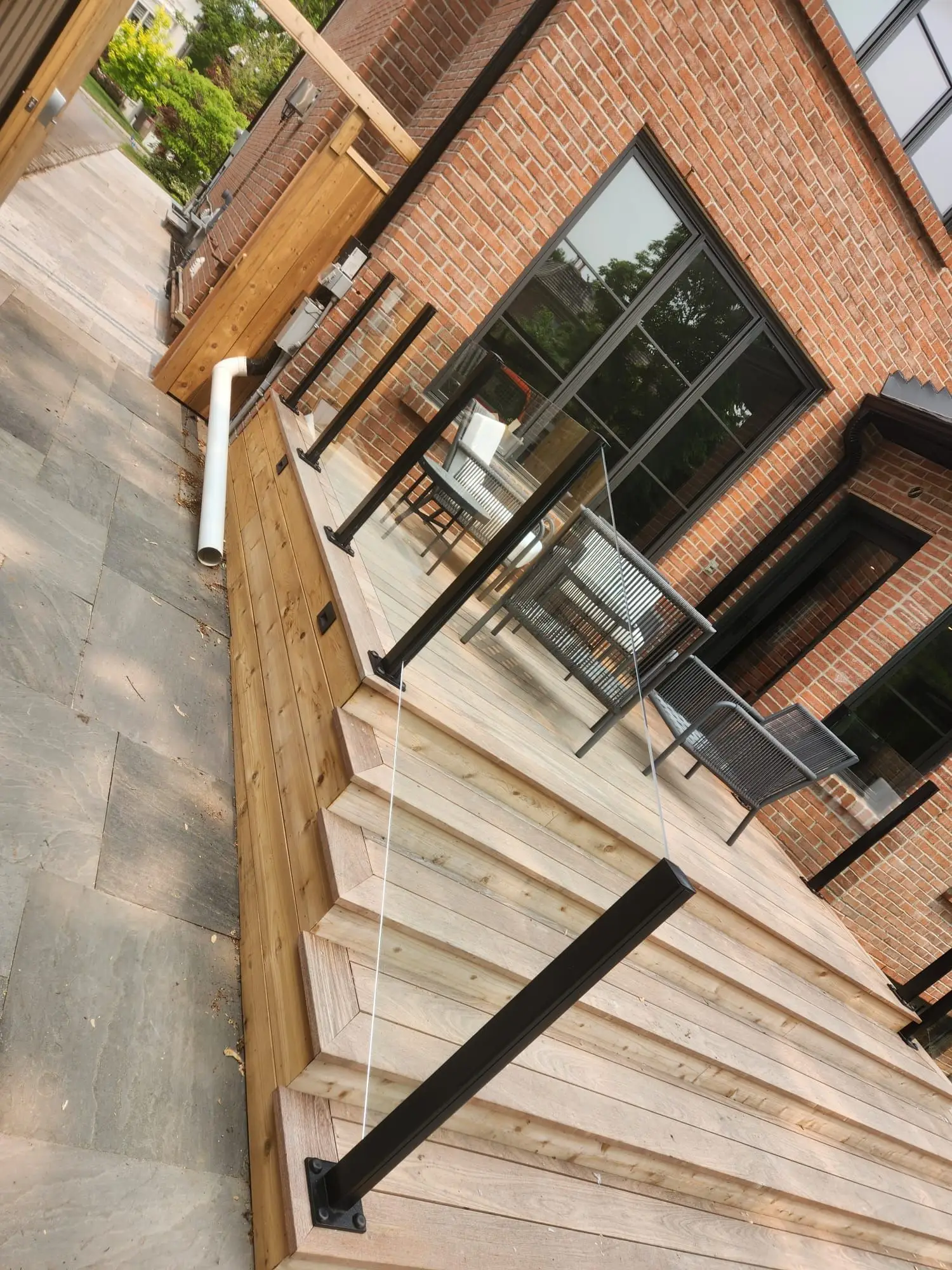 Frameless glass railing with black posts around a wood deck beside a brick house