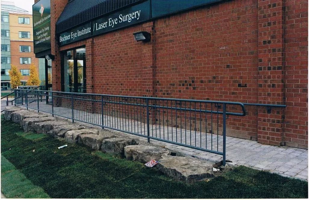 Black metal handrail running the length of a ramp along a brick commercial building