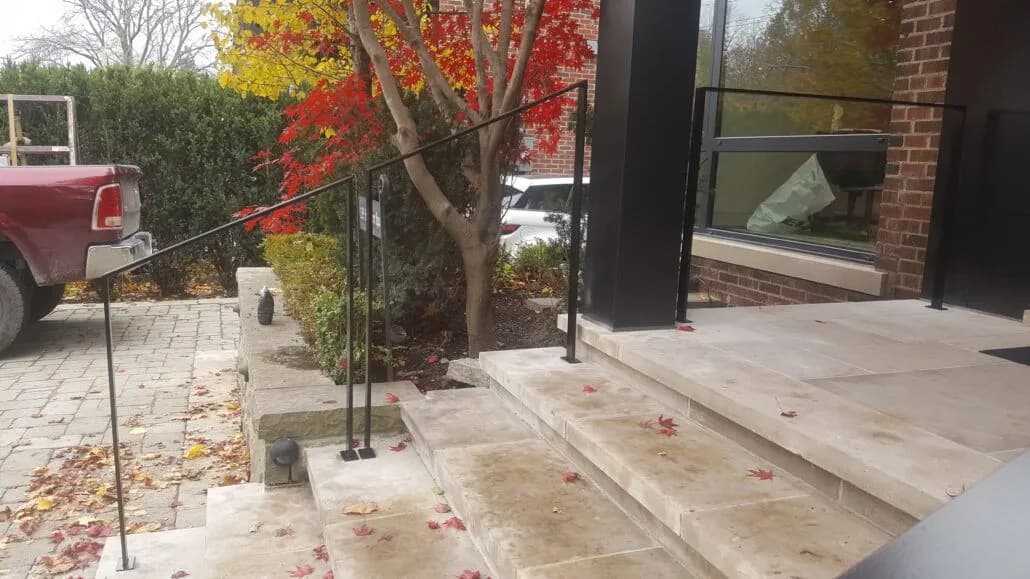 Slim black metal railing with thin posts along wide stone entrance steps in autumn