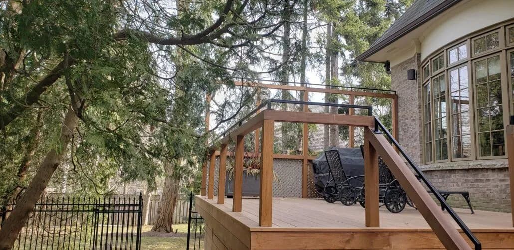 Dark railing along a raised wood deck with a ramp, beside a house among tall trees