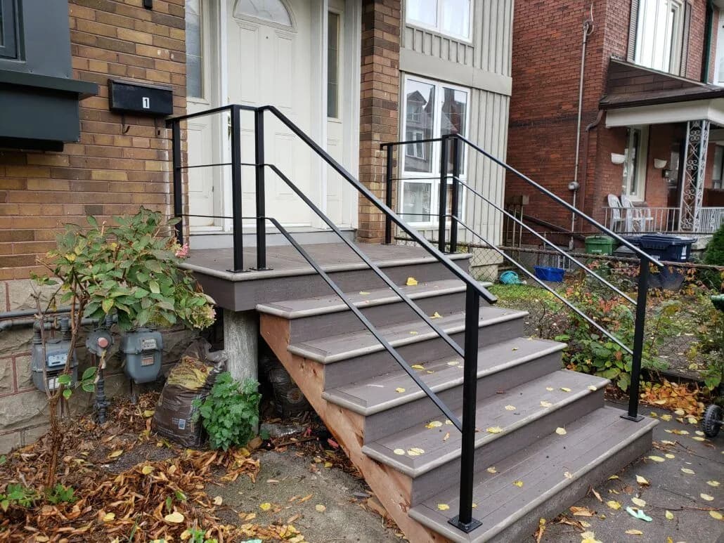 Black metal railing with horizontal rails along composite deck steps beside a brick house