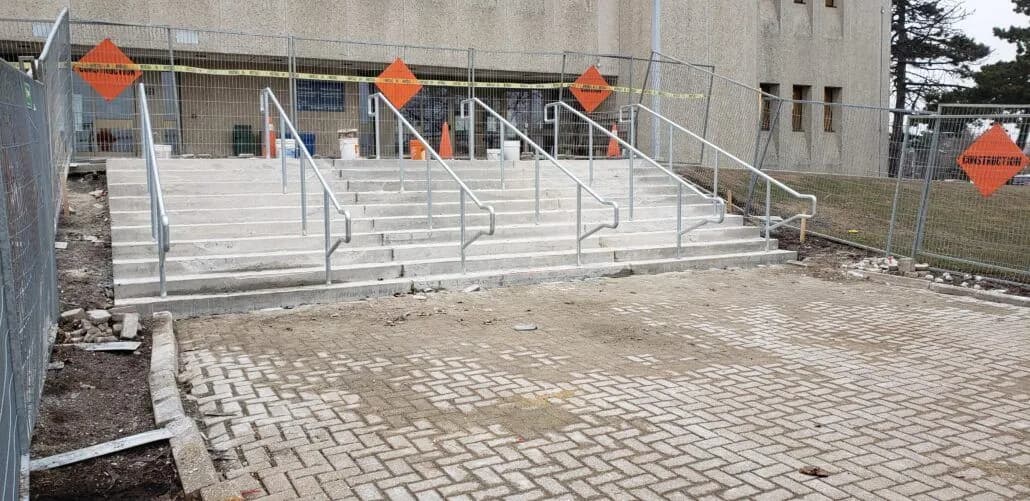 Galvanized steel handrails on wide concrete entrance steps, with site fencing still in front