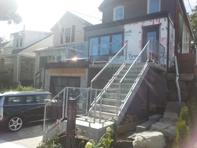 Glass railing with metal posts on a raised deck of a house still wrapped in building paper