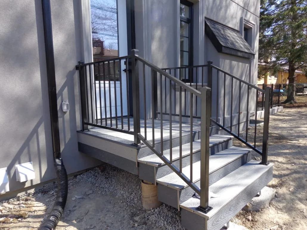 Black metal railing around a side entrance landing and steps beside a house