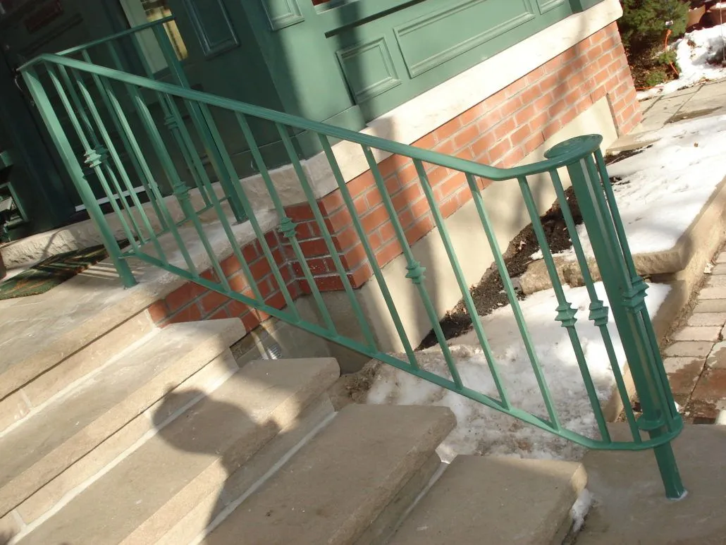 Green painted metal railing with turned balusters on concrete front steps in winter