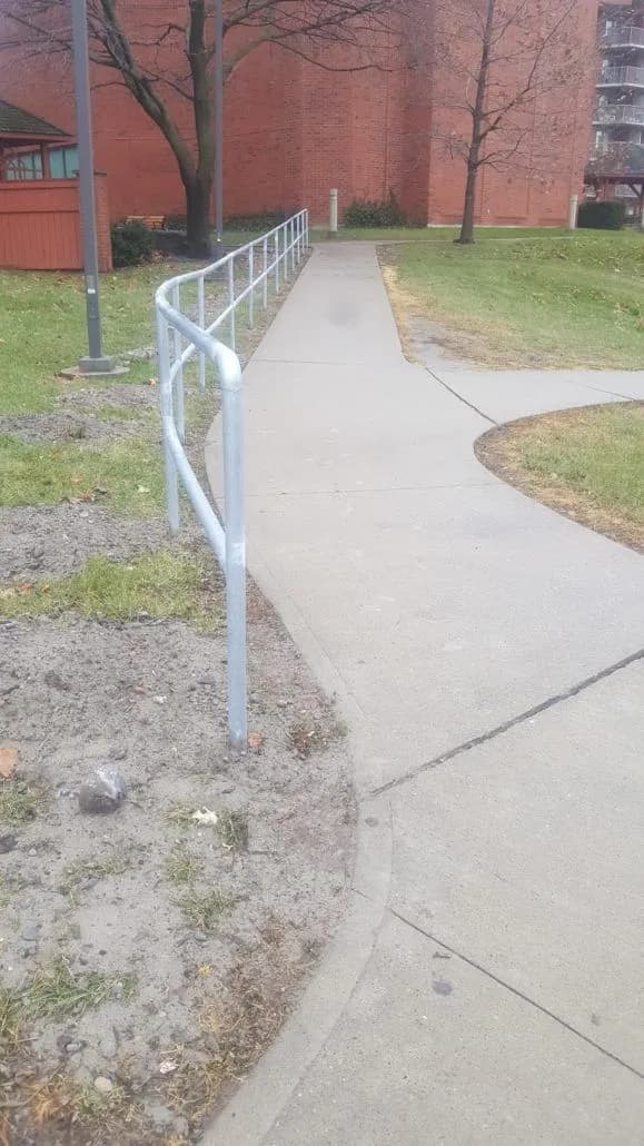 Galvanized steel handrail following a curving concrete walkway beside a brick building