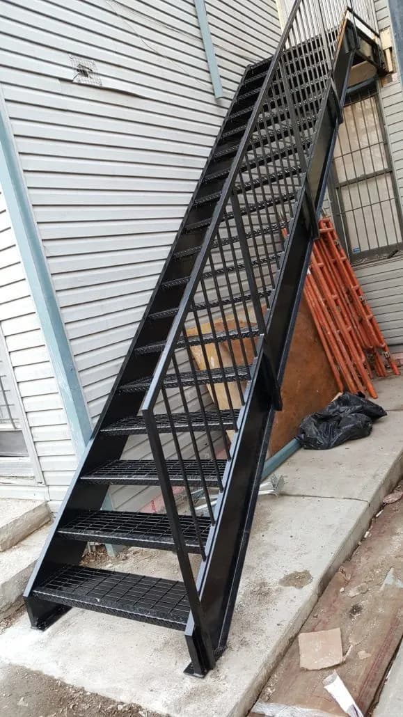 Straight black steel exterior staircase with open grating treads and picket railings running up the side of a house