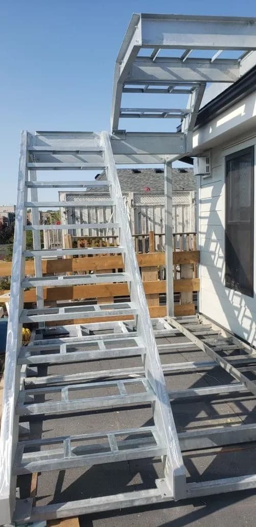 Galvanized steel exterior staircase with a mid-level landing and railings rising along the back of a house
